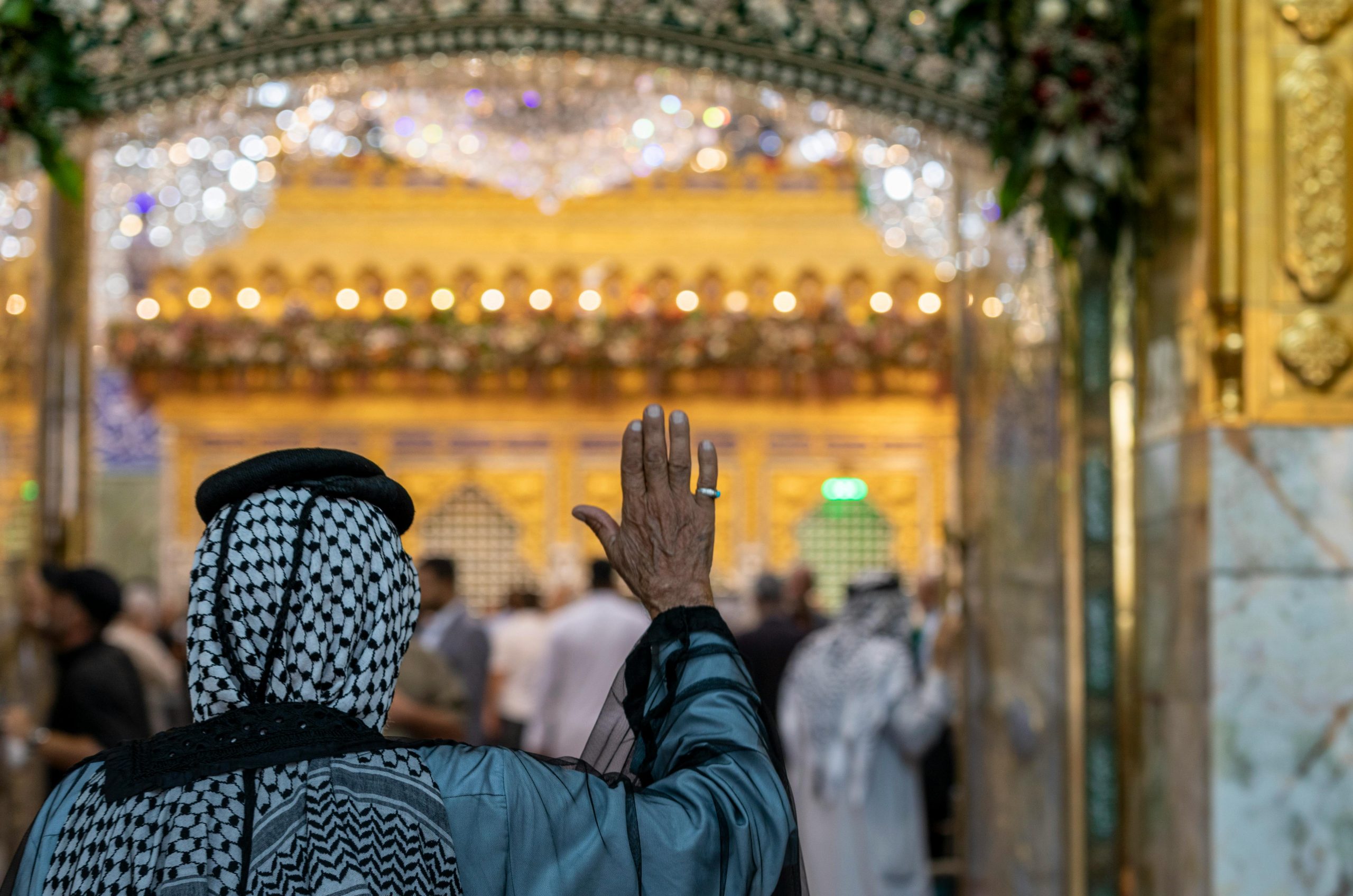A devotee raises a hand in prayer at a beautifully adorned shrine in Karbala, Iraq.